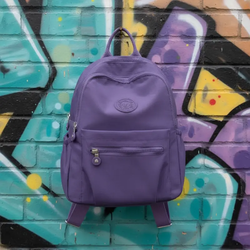 Purple nylon mini backpack hanging on graffiti brick wall