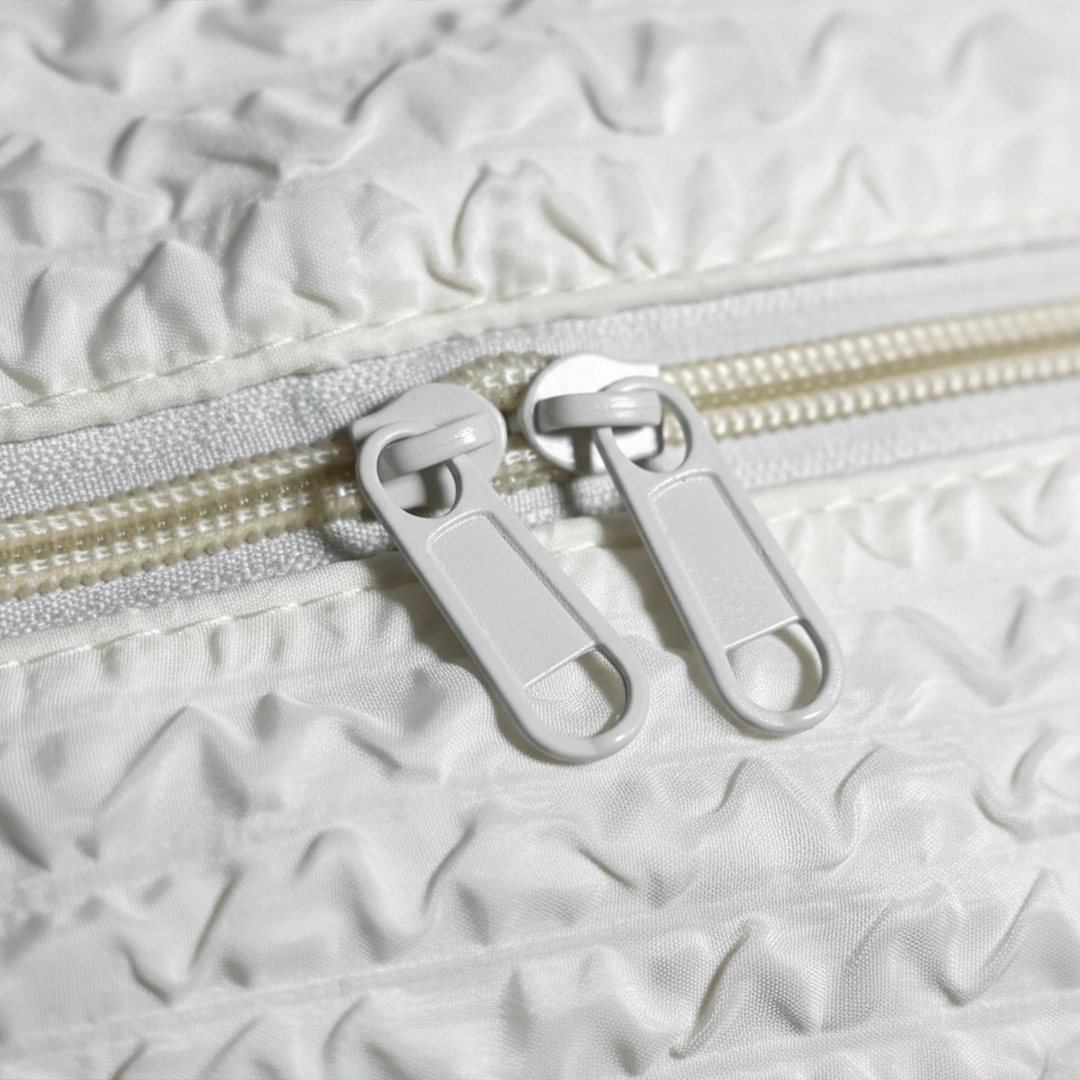 Close-up of TORTKART White Textured Backpack fabric, showing the unique bubble/crinkle texture and the durable, light-grey zipper pulls and teeth. Highlights premium quality material.