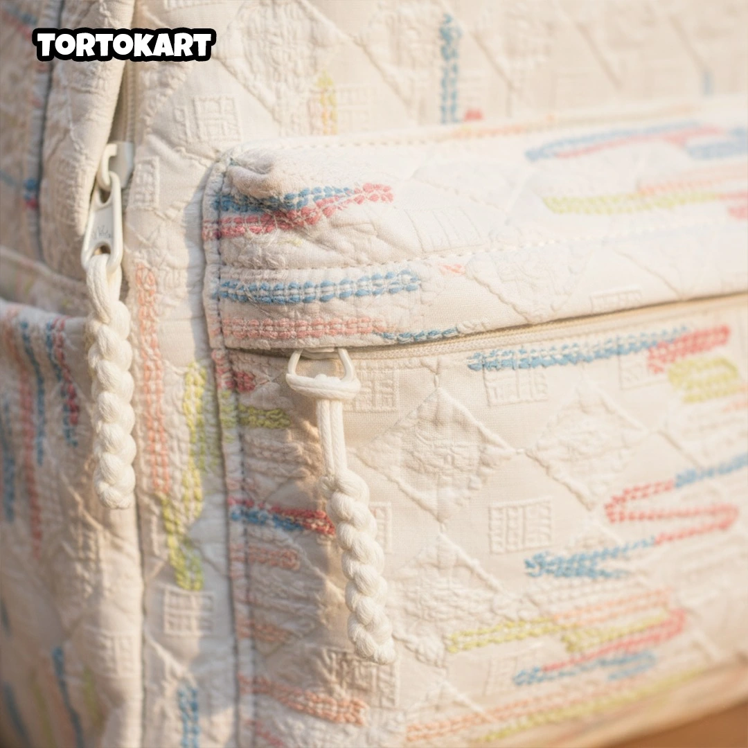 close-up detail of white quilted backpack fabric with colorful embroidered stitches and thick white rope zipper pulls