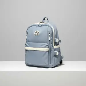 Color-blocked backpack in dusty blue and cream beige, featuring multiple zippered compartments, front buckle straps, and utility side pockets, styled with a rolled map and sunglasses.