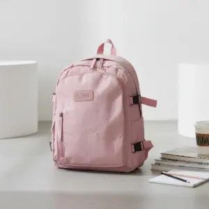 Pink water-resistant backpack with visible water droplets and a "FASHION" patch, sitting on a floor next to a stack of books and a coffee cup.