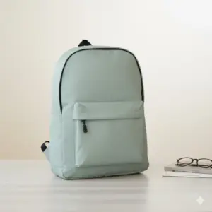 Aesthetic light sage green or mint backpack with a minimalist design, featuring a large front zip pocket and black trim, displayed on a light wooden table next to a stack of books and glasses.