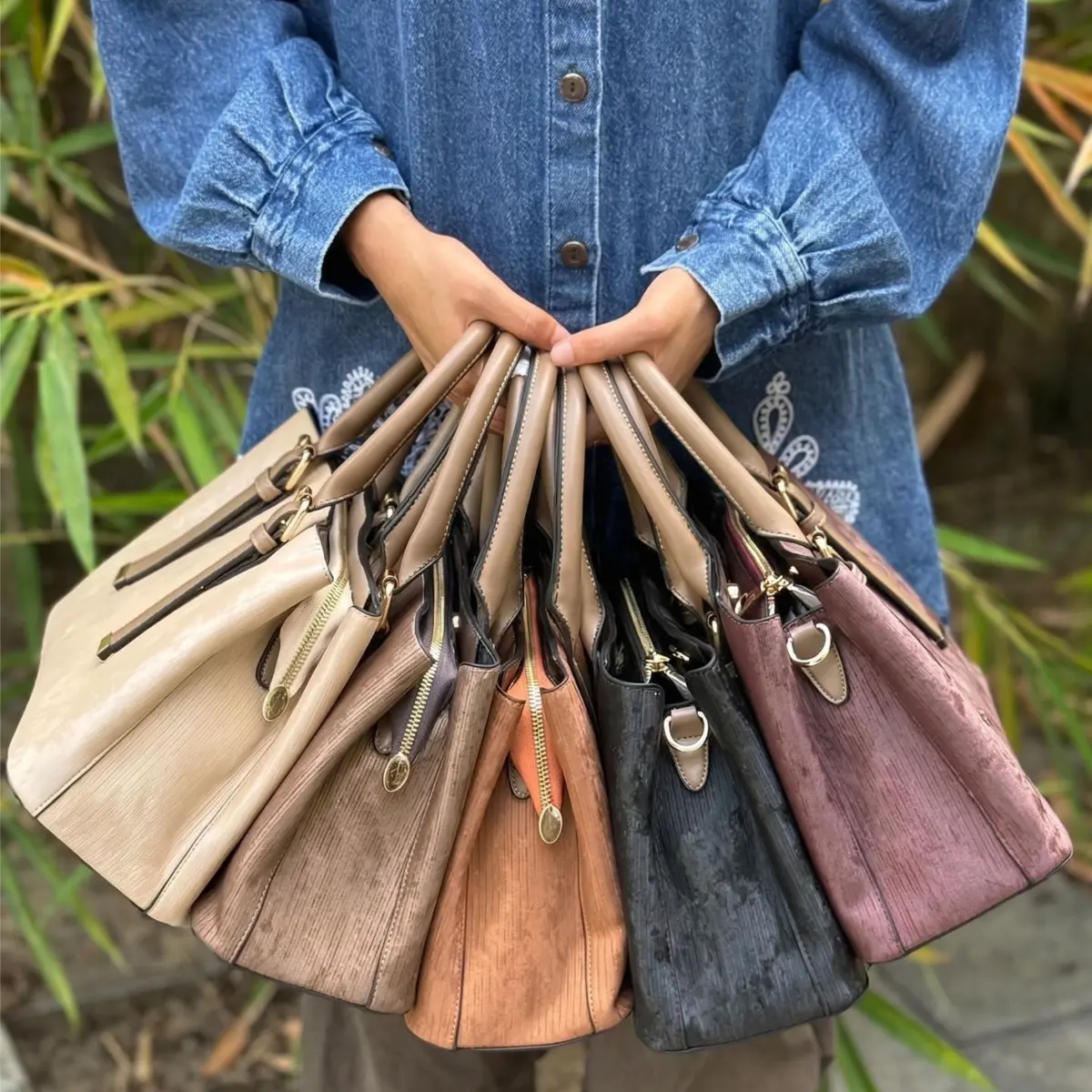 A premium women's handbag in deep navy blue featuring a vertical pleated texture and polished gold-tone hardware, held by a woman in a matching navy blue pleated dress with gold jewelry.