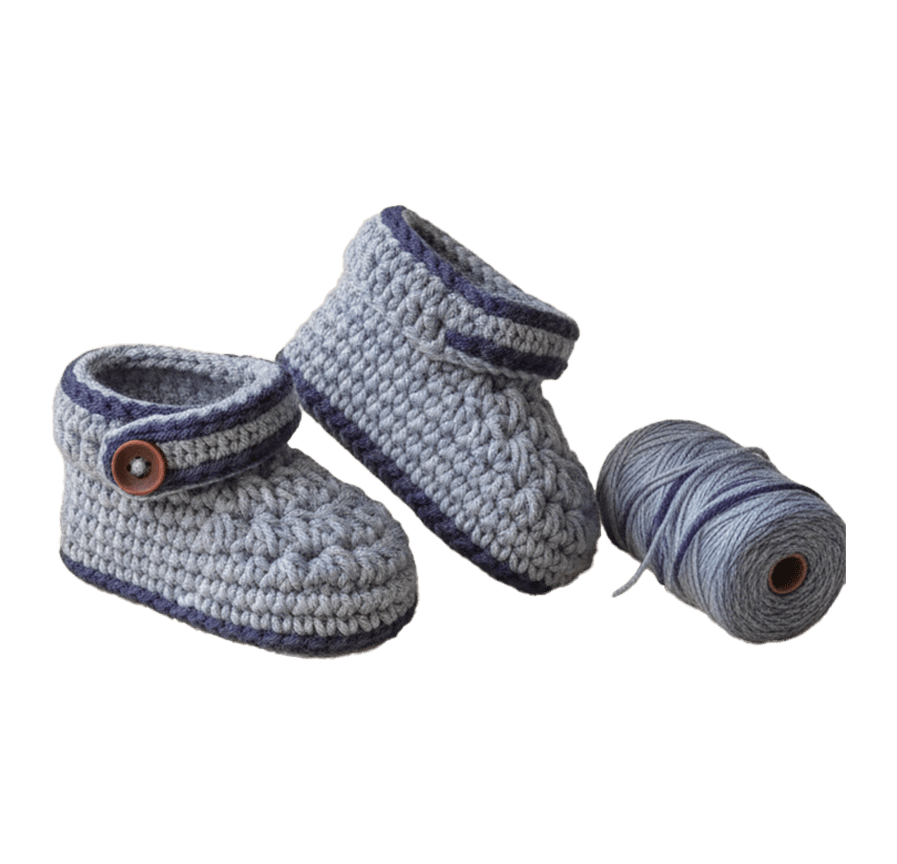 A pair of handmade light blue and grey crochet baby booties with navy blue trim and a brown button detail, shown next to a matching spool of yarn against a solid black background.