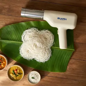 Automatic handheld electric idiyappam maker by Buarn placed on a wooden surface next to fresh string hoppers on a banana leaf with vegetable curry and chutney.