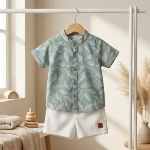 A baby boy summer clothing set hanging on a wooden hanger, featuring a sage green half-sleeve button-up shirt with a white leaf print and a mandarin collar, paired with textured white shorts.