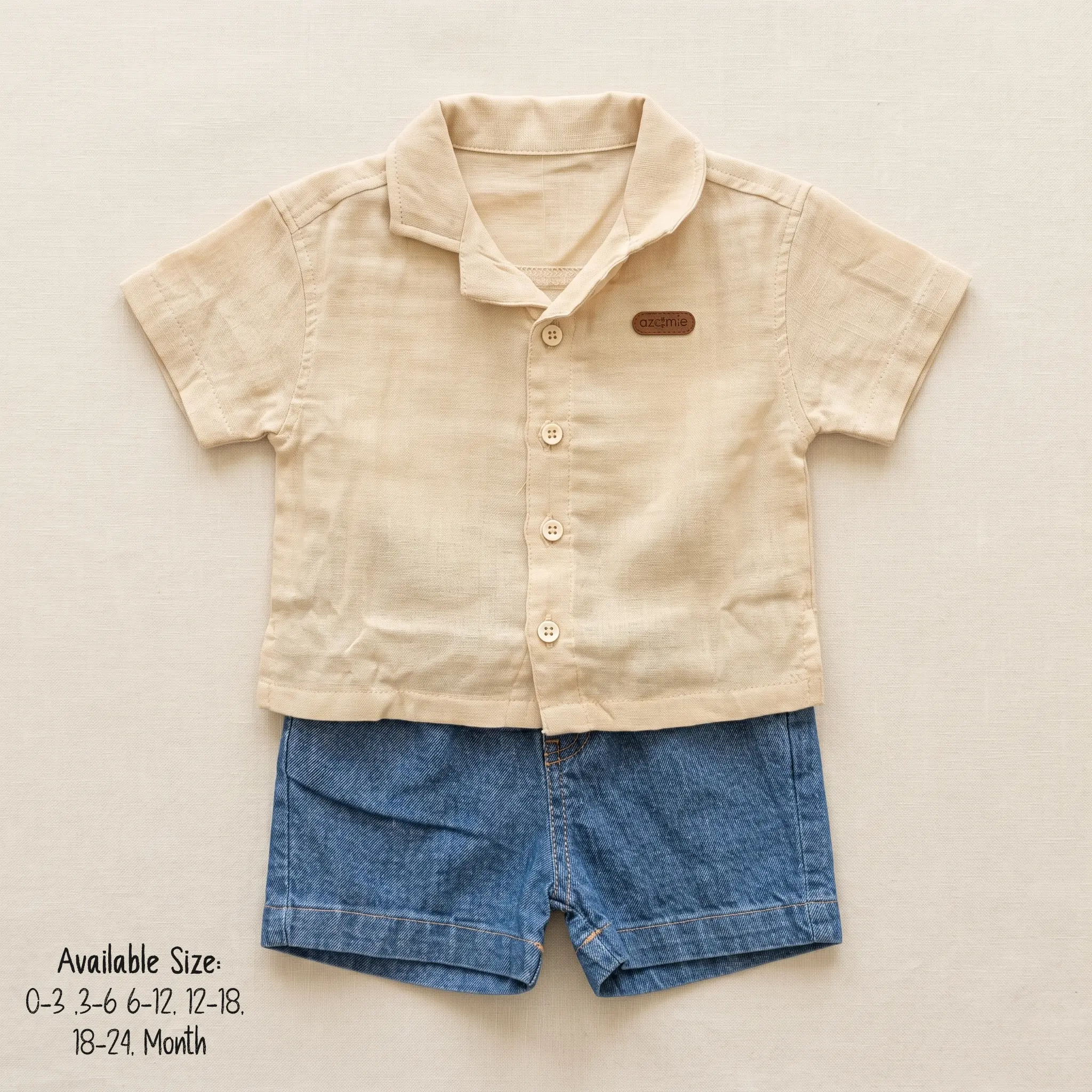 A casual baby boy summer clothing set laid flat on a light beige background, featuring a beige half-sleeve button-down shirt with a notch lapel collar, paired with classic blue denim jean shorts.