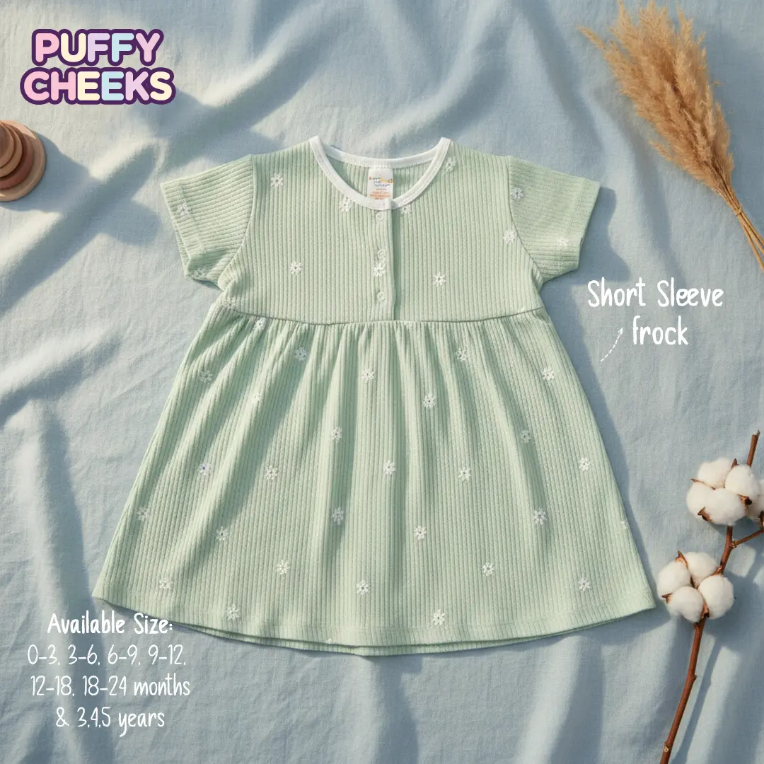 The image displays a mint green ribbed waffle-knit baby frock patterned with small white flowers, short sleeves, a gathered waist, and a white trim collar, laid flat on a light blue fabric background next to a cotton pod branch and dried pampas grass, featuring text overlays for Puffy Cheeks branding and available sizes.