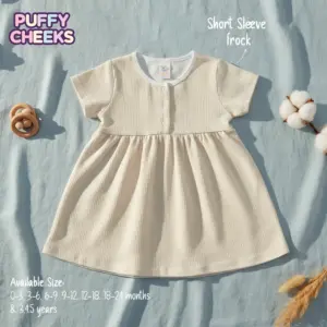 The file 3 (15).webp displays a cream-colored waffle knit baby frock with short sleeves, a gathered waist, and three buttons at the neck, laid flat on a light blue fabric background next to a wooden rattle, a cotton pod, and dry grass, featuring text overlays for Puffy Cheeks branding and available sizes.
