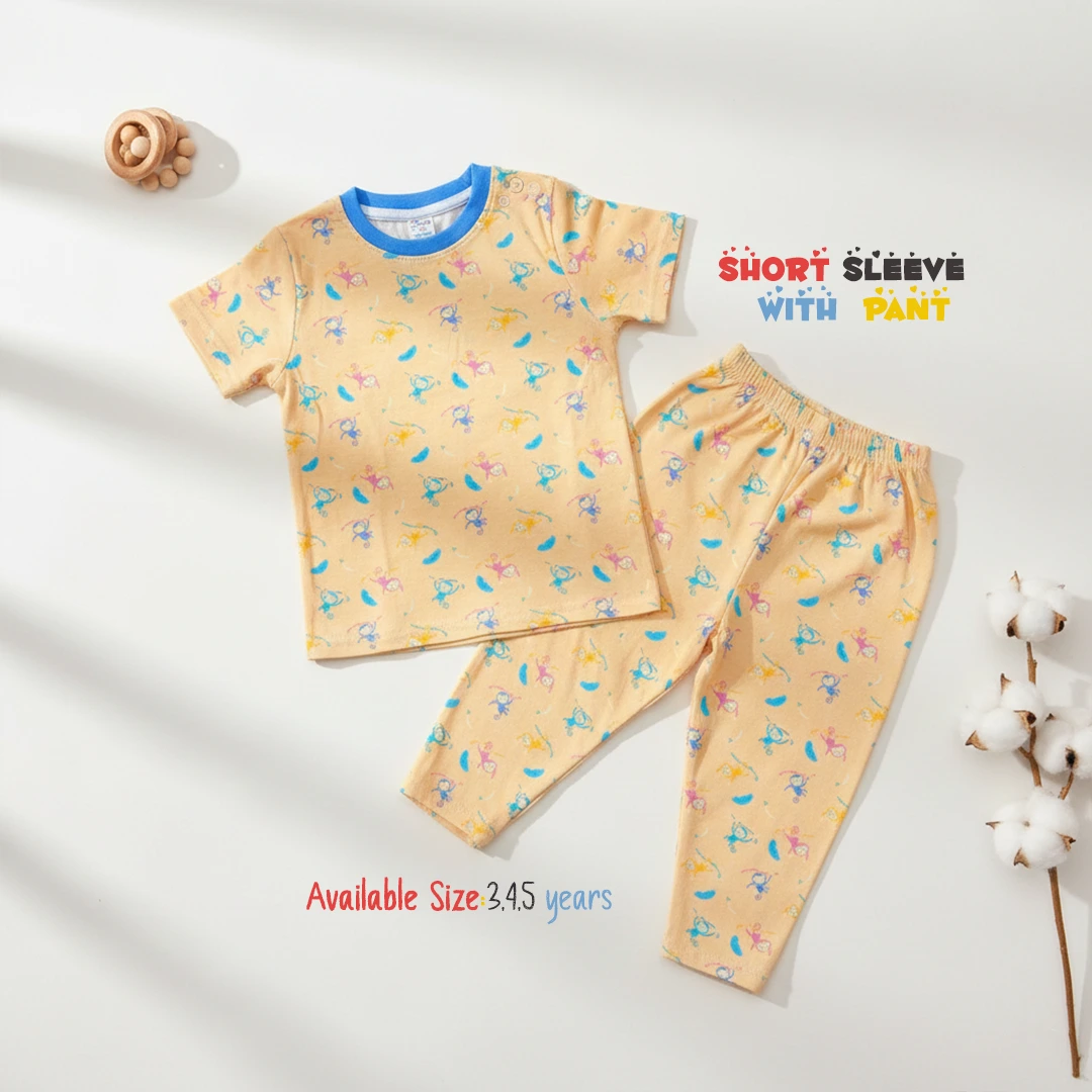 The image displays a soft peach or light orange toddler lounge set covered in a colorful print of small cartoon monkeys and bananas, consisting of a short sleeve round neck t-shirt with a bright blue collar trim and matching long pants, laid flat on a white surface next to a wooden toy and a cotton branch.