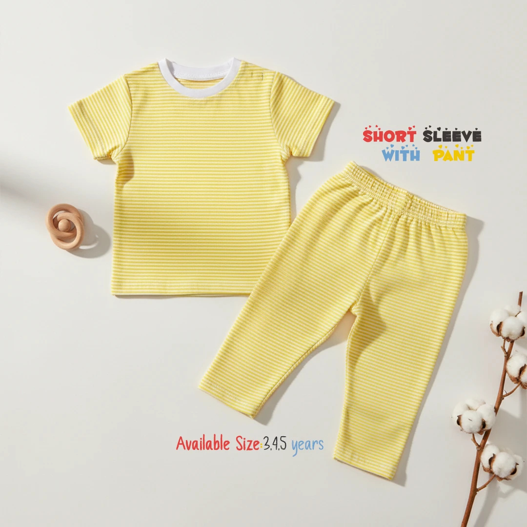 The image displays a soft yellow and white horizontally striped toddler lounge set, consisting of a short sleeve round neck t-shirt with a solid white collar trim and matching long pants, laid flat on a white surface next to a wooden rattle toy and a cotton branch.
