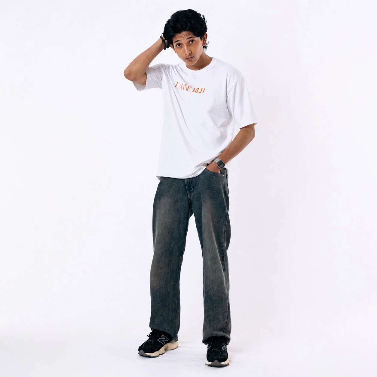 The primary goal of Alt Text is accessibility and image search optimization. It should clearly describe the image while weaving in high-value search terms naturally. Suggested Alt Text: Young man posing in the Laynered Premium White Loop Knit Drop-Shoulder Streetwear Tee paired with faded dark grey baggy jeans and black sneakers against a clean white studio background.