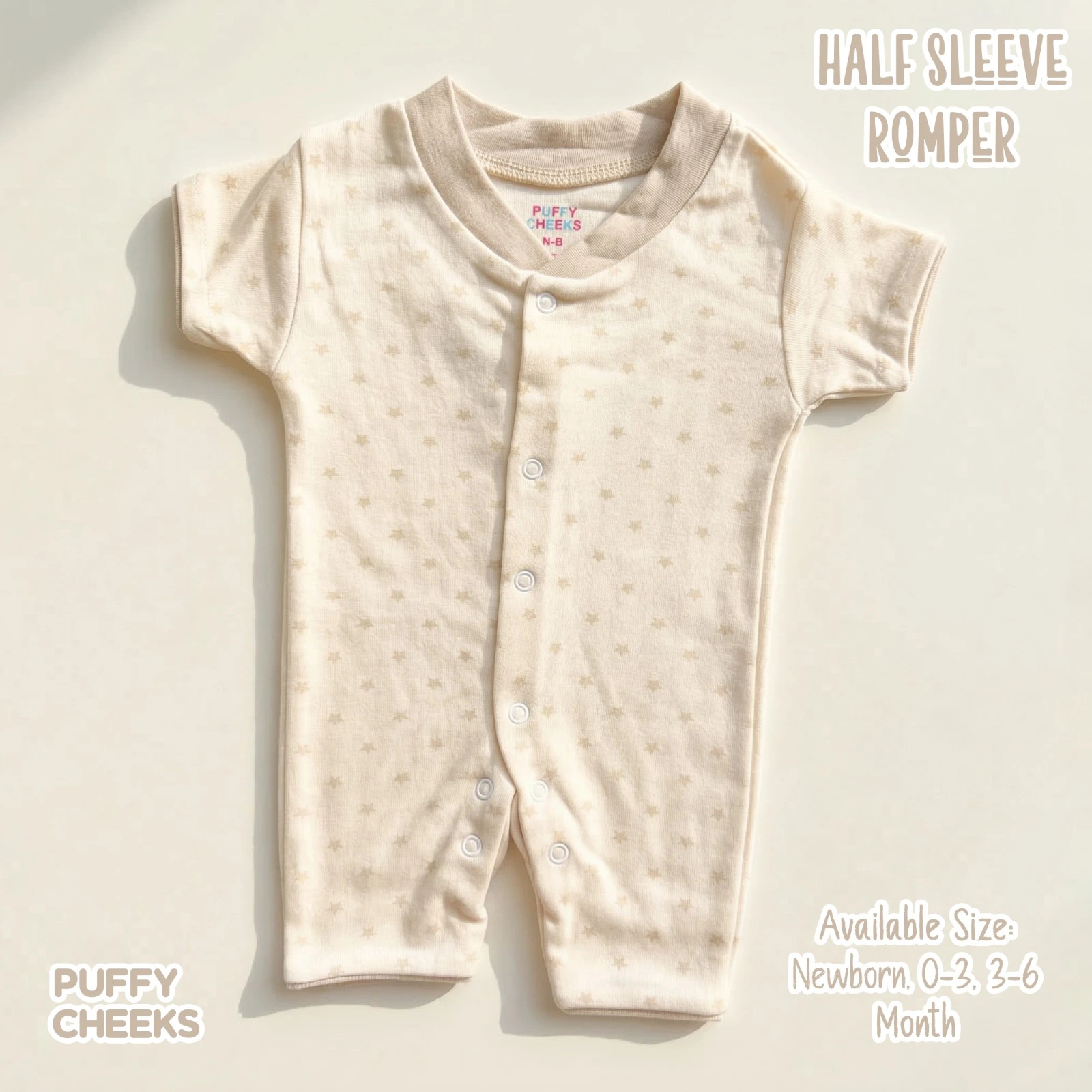 The image shows a cream-colored, half-sleeve baby romper by Puffy Cheeks featuring an all-over faint star print. The garment is designed with a beige ribbed collar, short sleeves, a full asymmetric snap-front closure running down to the left leg, and crotch snaps, flat-laid on a smooth cream surface under soft natural lighting.