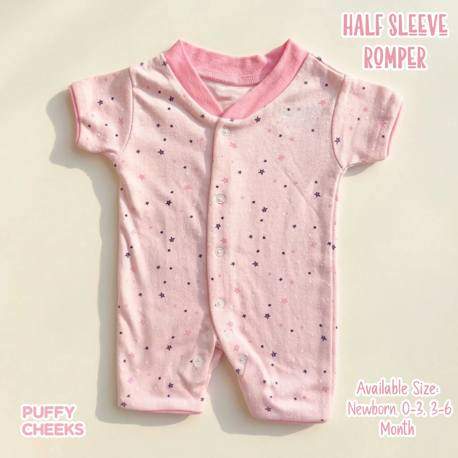 Half sleeve baby romper by Puffy Cheeks featuring an all-over tiny scattered star pattern in dark purple and deep pink on a light pink cotton fabric, designed with a thick pink overlapping v-neck ribbed collar, short sleeves, a full snap-button front closure, and snaps along the crotch inseam, displayed flat on a clean cream surface.