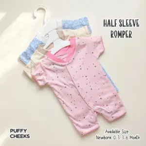 The image displays a 3-piece bundle of half-sleeve baby rompers by Puffy Cheeks neatly arranged on white plastic hangers. The top romper is baby pink with a scattered dark purple and pink star pattern and a bright pink collar. Layered behind it are the other two rompers from the wholesale set: a cream romper with a soft star pattern and a light blue romper with a white geometric snowflake pattern, all flat-laid on a clean cream-colored background.