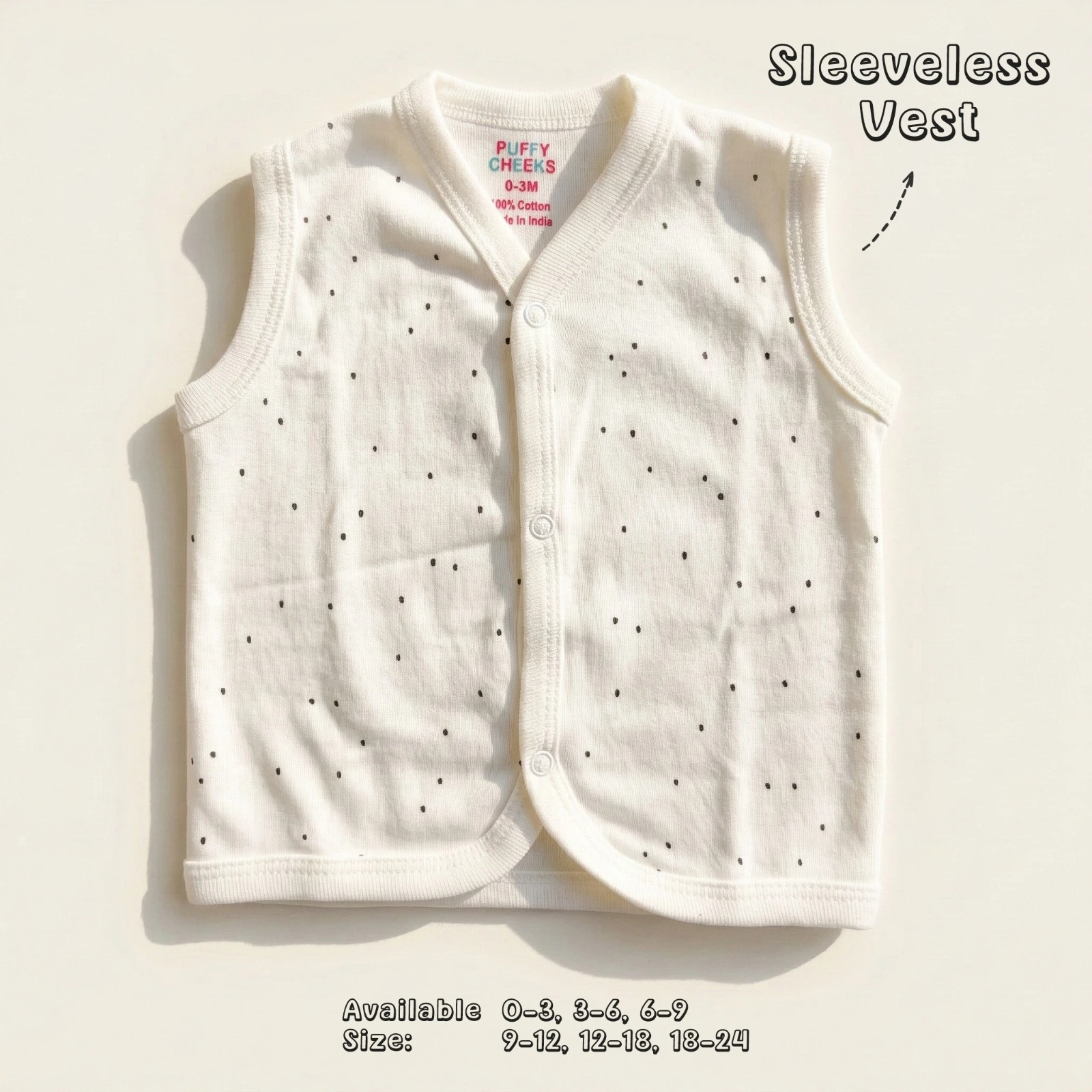 The image shows a cream-colored sleeveless baby vest by Puffy Cheeks with a v-neckline and snap-button front closures. The vest features a minimalist all-over black polka dot print pattern, laid flat on a smooth white surface.
