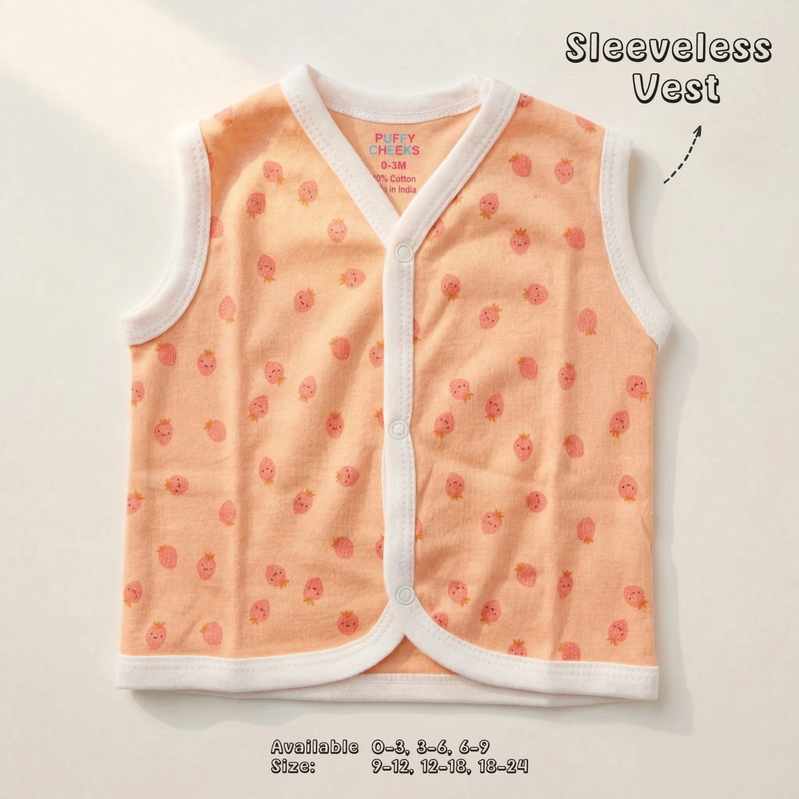 The image shows a light peach-colored sleeveless baby vest by Puffy Cheeks with a white v-neckline trim and snap-button front closures. The vest features a cute all-over print of tiny pink strawberries with little green stems, laid flat on a smooth white surface.