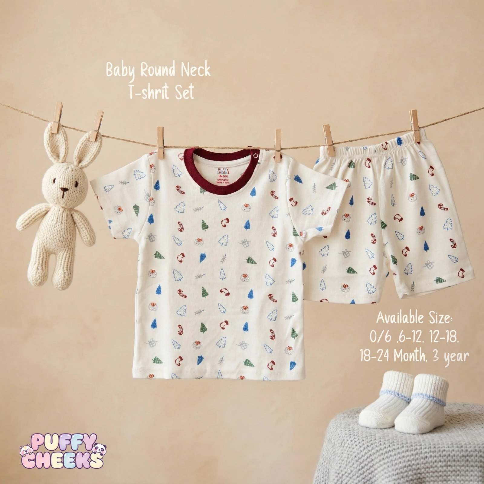 Baby round neck t-shirt and shorts set by Puffy Cheeks featuring an all-over Christmas holiday print with green, blue, and white pine trees, red candy canes, and stockings on soft cream cotton fabric, with the short-sleeve t-shirt showing a dark maroon red crew neck collar and a left-shoulder snap button, hanging from a clothesline with wooden pegs next to matching elastic-waist shorts and a small knit bunny toy, displayed above white knit infant booties with blue trim on a grey blanket.